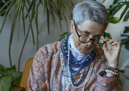 Confident mature woman with silver hair and layered pearls lowering her glasses — celebrating natural beauty and the pro-ageing movement with AYA Natural Skin"