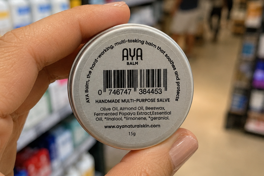 Hand holding AYA Balm tin showing ingredient label in South African pharmacy — natural skincare with raw fermented papaya