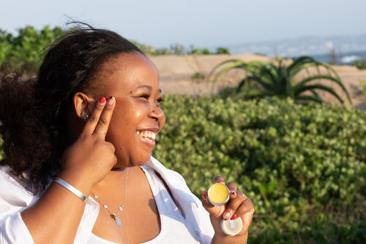 oman applying natural face balm to her cheek outdoors, holding an open tin of AYA Balm as an alternative to traditional moisturiser
