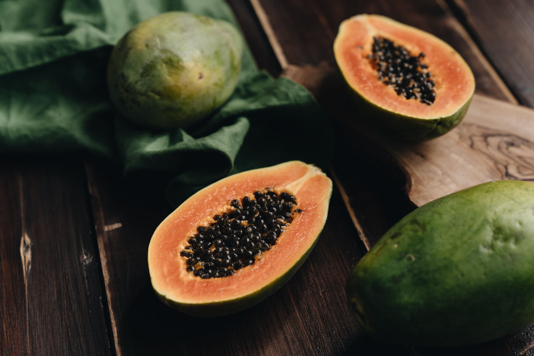 Ripe papaya (pawpaw) cut in half showing orange flesh and black seeds on a wooden table